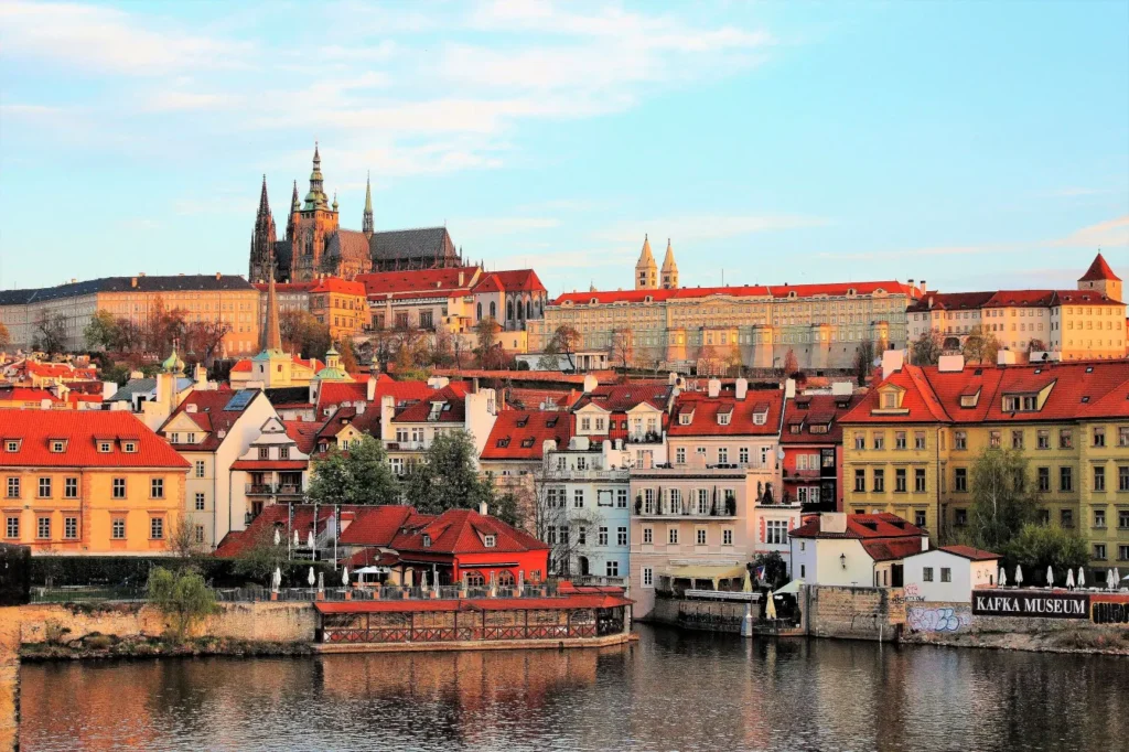 Panorama Pražského hradu s katedrálou sv. Víta, pohled na červené střechy Malé Strany a Vltavu za slunečného dne.