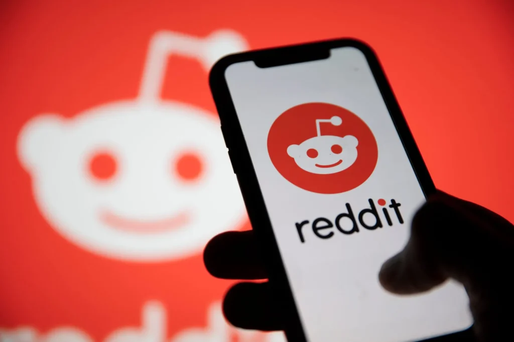 Aplikace Reddit na mobilním telefonu s červeným logem na pozadí, představující přístup k online diskuzím a sdílení obsahu.