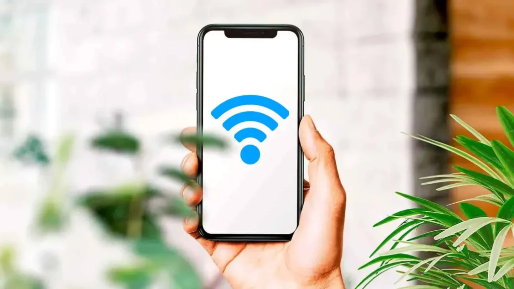 Osoba držící iPhone s ikonou Wi-Fi na displeji, ilustrující sdílení hesla k Wi-Fi pomocí moderních metod jako Bluetooth nebo QR kódu.