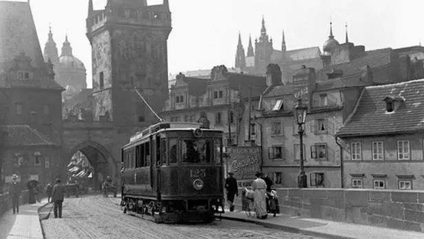 Dobová fotografie Karlova mostu se starou tramvají a pěšími chodci, zachycující atmosféru Prahy v první polovině 20. století.