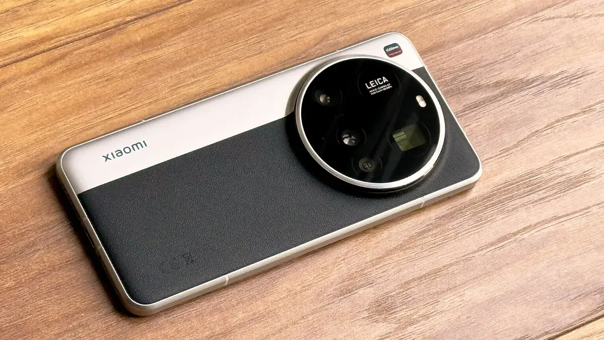 Zadní strana Xiaomi 15 Ultra s velkým kruhovým modulem fotoaparátu Leica a elegantním designem kombinujícím kov a koženku, položený na dřevěném stole.