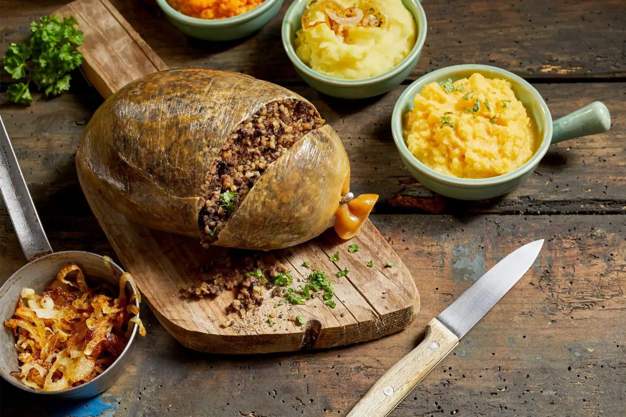 Tradiční skotský pokrm haggis servírovaný na dřevěném prkénku s přílohou bramborové kaše a tuřínového pyré.