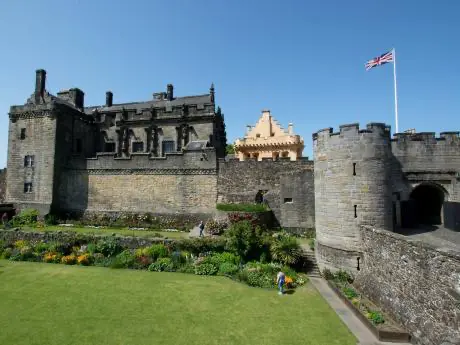 Impozantní skotský hrad Stirling Castle obklopený zelenými zahradami a s britskou vlajkou vlající nad věží.